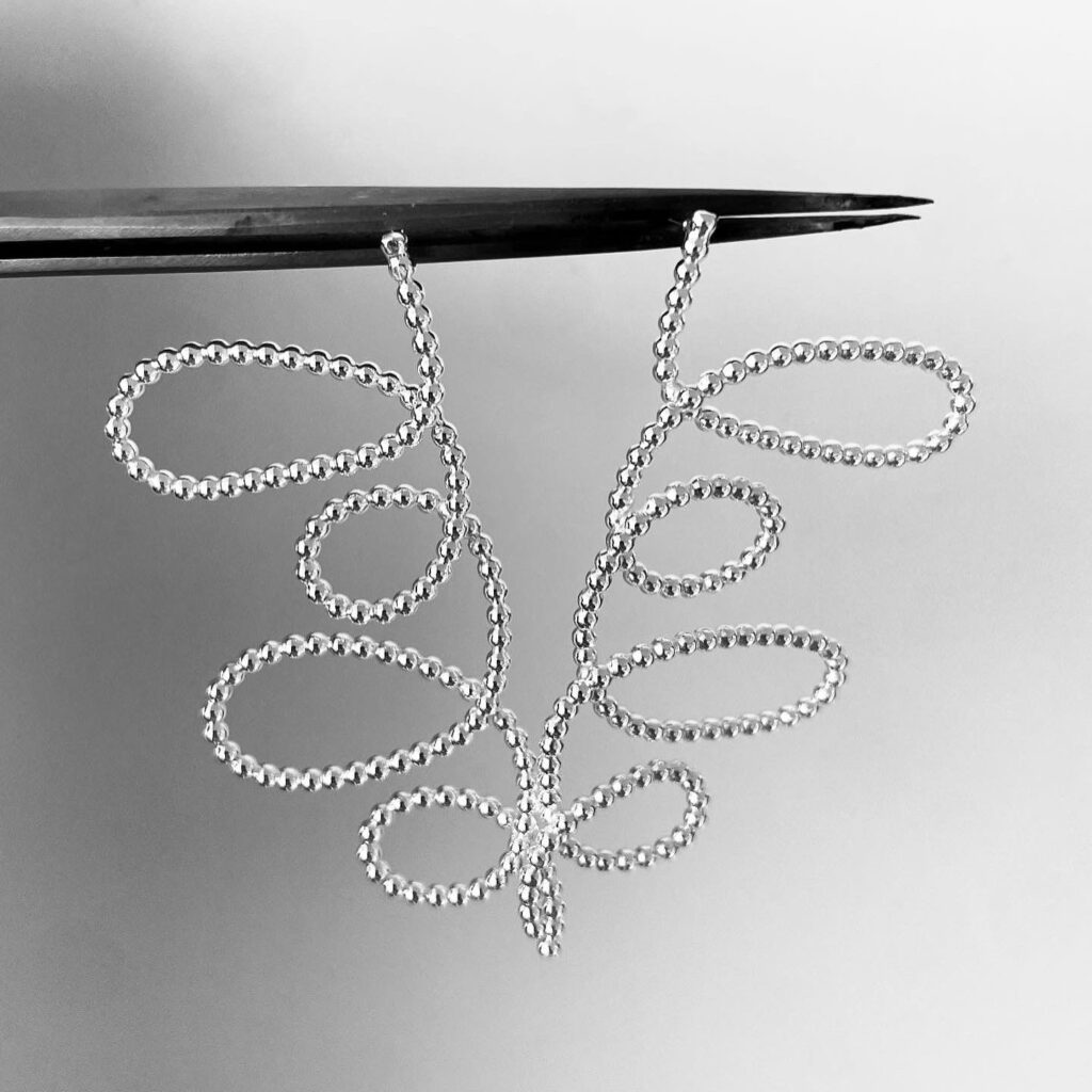 A tweezer holding a pair of silver earrings shaped as loops of dotted silver wire