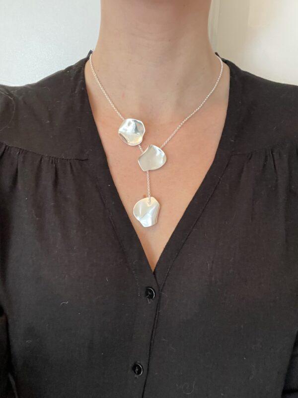 A woman with a black shirt wearing a silver necklace with three silver rose petals