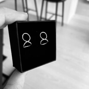 A blck jewelry box with a pair of handmade silver earrings shaped as eternity symbols with a little bend