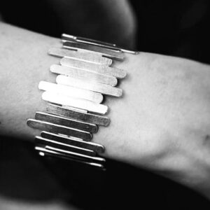 A wrist wearing a handmade silver bracelet shaped as sticks put together randomly