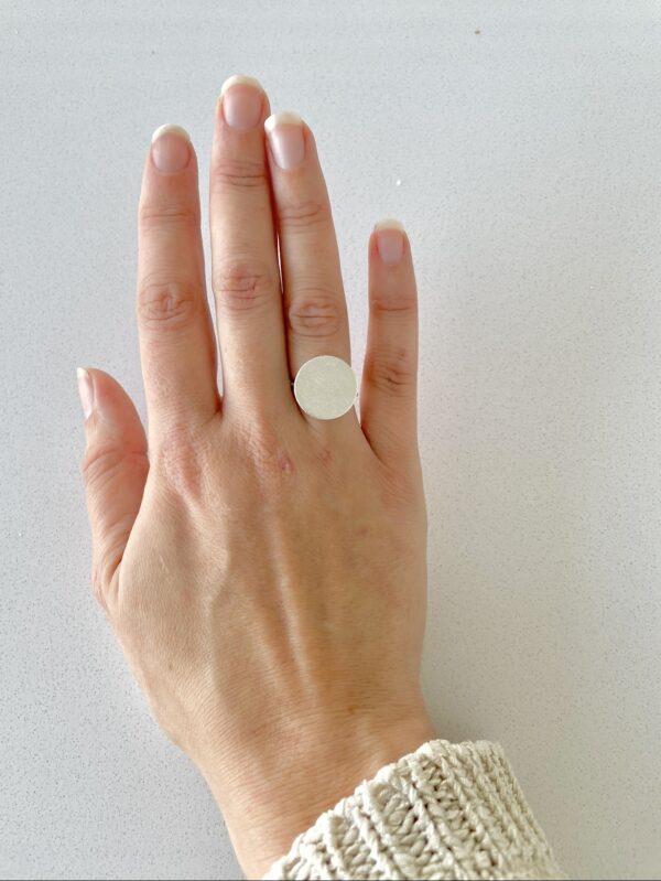 A hand wearing a matte handmade silverring shaped as a coin.
