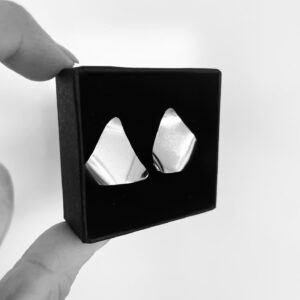 Two fingers holding a black jewelry box showing two silver earrings shaped as wavy triangles,