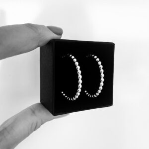 Two fingers holding a black jewelry box with a pair of silver hoops