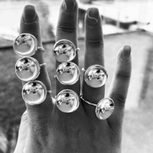 A hand wearing 8 handmade silverrings shaped as bowls with a matte inside