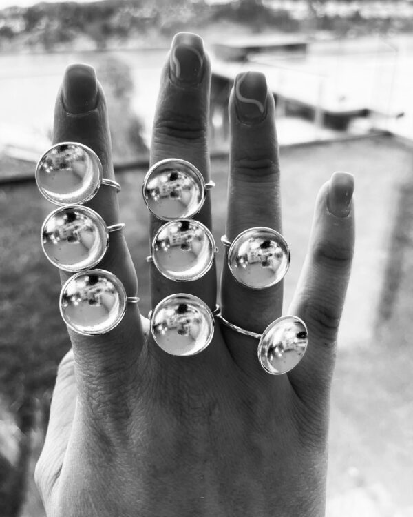 A hand wearing 8 handmade silverrings shaped as bowls with a matte inside