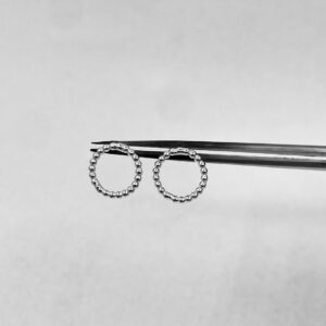 A tweeze holding a pair of silver earrings shaped as shiny rings