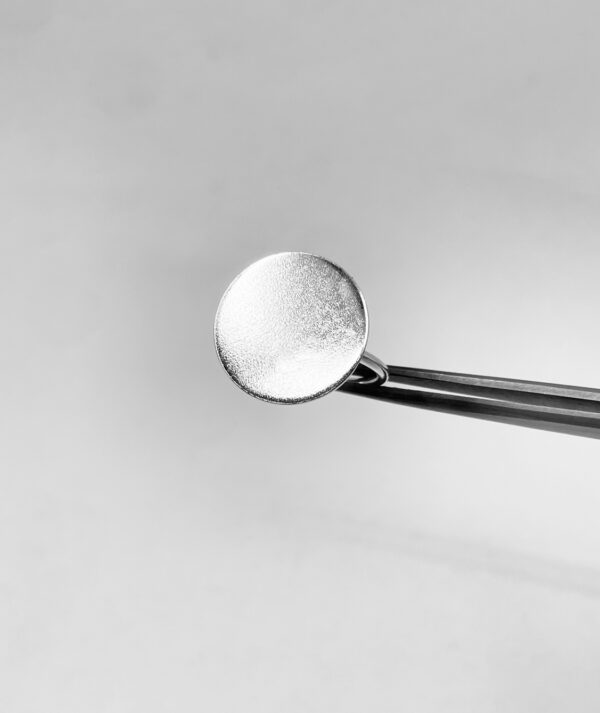 A tweezer holding a silver ring shaped as a matte coin