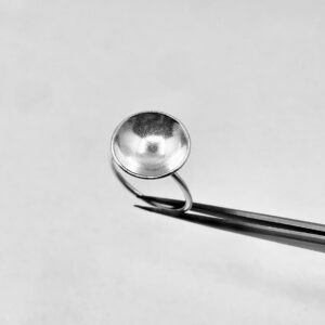 A tweezer holding a handmade silver ring shaped as a bowl.
