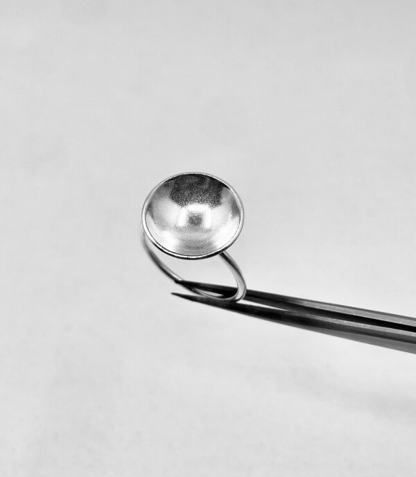 A tweezer holding a handmade silver ring shaped as a bowl.