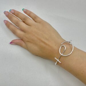 A wrist wearing a silver bracelet shaped as a venus symbol