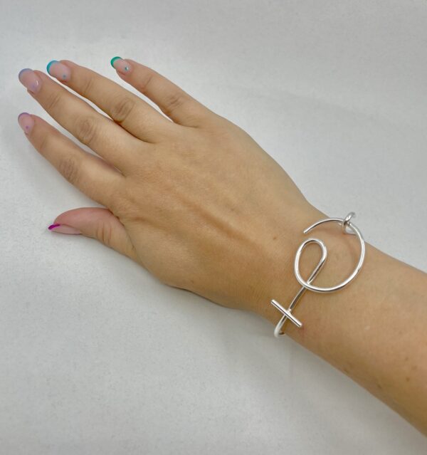A wrist wearing a silver bracelet shaped as a venus symbol