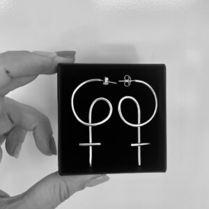 Two fingers holding a black jewelry box with a pair of silver earrings shaped as venus symbols,