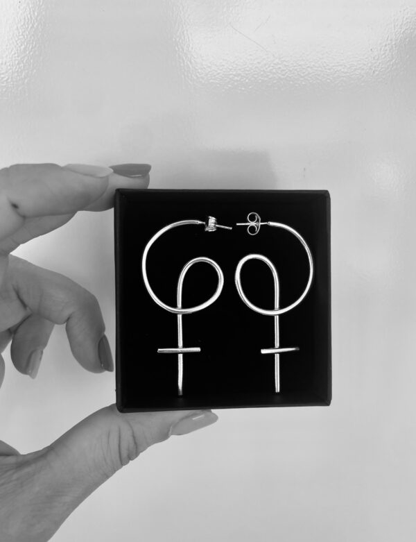 Two fingers holding a black jewelry box with a pair of silver earrings shaped as venus symbols,