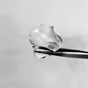 A tweezer holding a handmade silver ring shaped as a rose petal