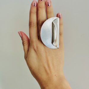 A hand wearing a handmade silver ring shaped as a big coin with on side folded.