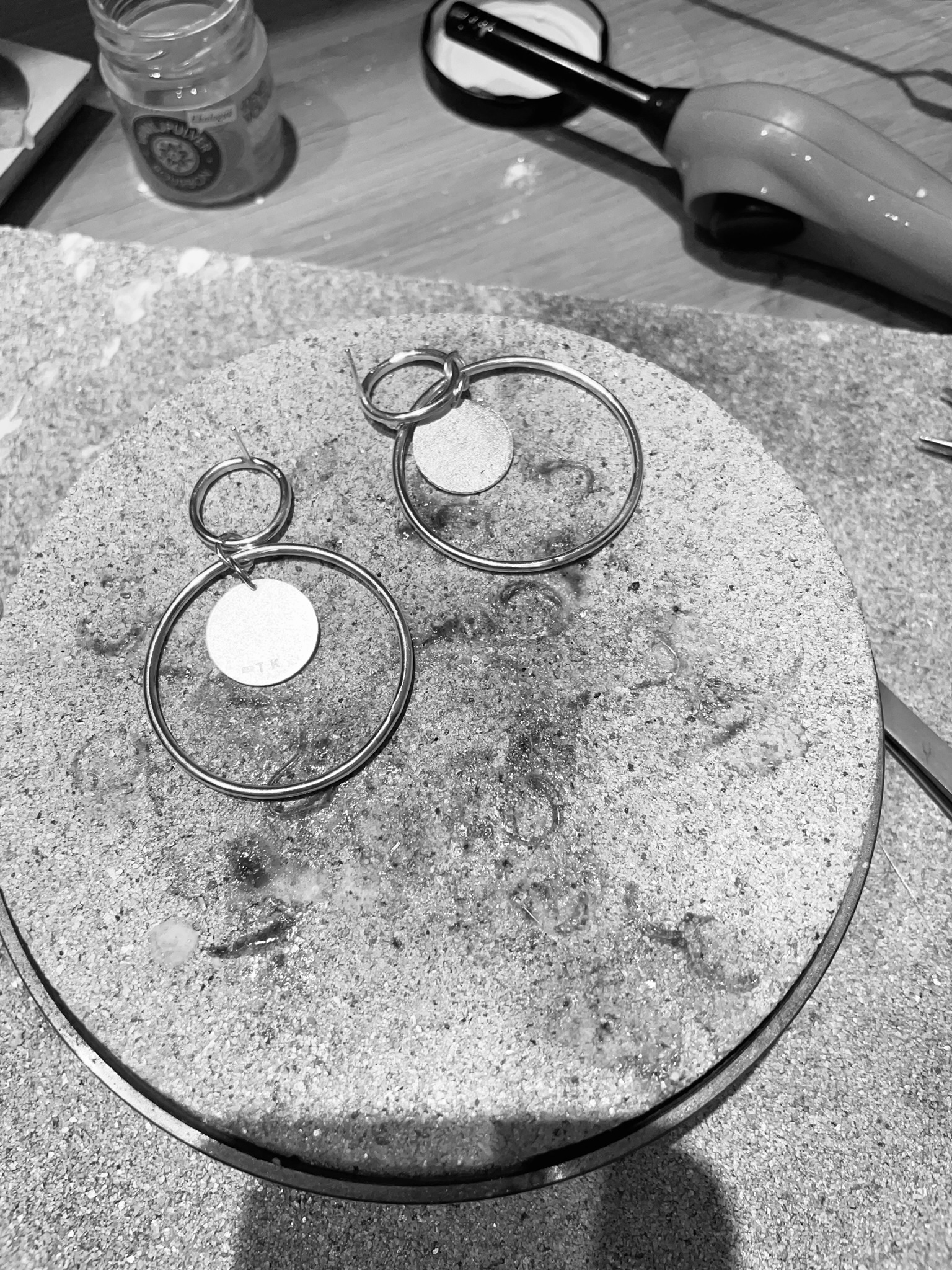 Two big earrings of silver circles put togehter on a silversmith's bench