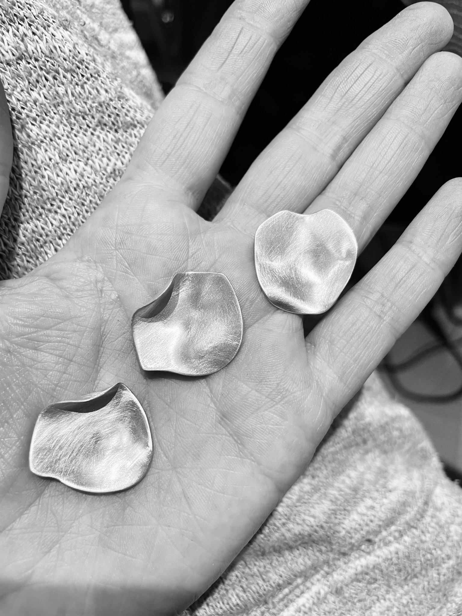 A hand holding three almost finished silver rose petals