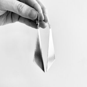 A hand holding a pair of hanging silver earrings shaped as triangles