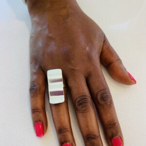 A hand with pink nail polish wearing a silver ring shaped as a wavy recctangle
