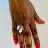 A hand with pink nail polish wearing a silver ring shaped as a wavy traingle