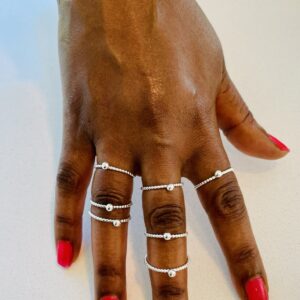 A hand with pink nail polish wearing7 thin silverrings with small dots