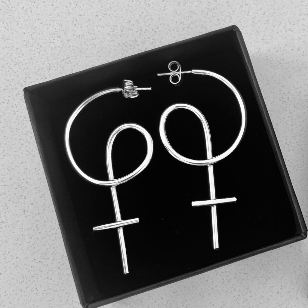 A black jewelry box with a pair of silver earrings shaped as venus symbols,
